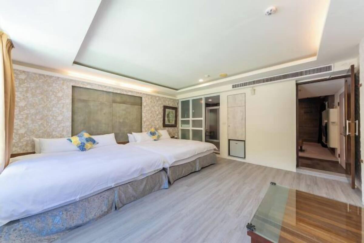 A bedroom with two beds, a large window, and a sliding door leading to a bathroom.