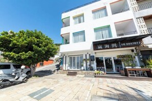 A multi-story hotel with a storefront, a tree in front, and a parked scooter. - Kenting Lan Bay Hotel (Pingtung)