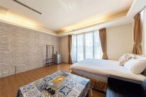 Une chambre d’hôtel moderne avec un mur d’accent en briques, un grand lit avec du linge de lit blanc, une table de chevet avec une boîte de mouchoirs et un radiateur portatif.