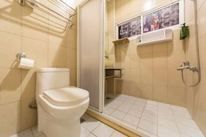 A bathroom with a toilet, a shower, and a small shelf with pictures. - Kenting Lan Bay Hotel (Pingtung)