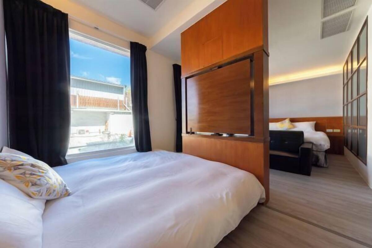 A hotel room with a large bed, a smaller bed, a wooden panel wall, and a window with curtains.