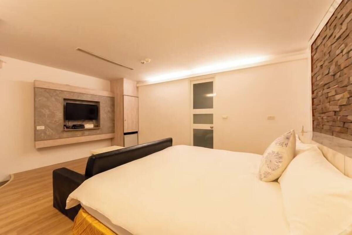 A modern bedroom with a bed, a TV mounted on the wall, and a wardrobe.