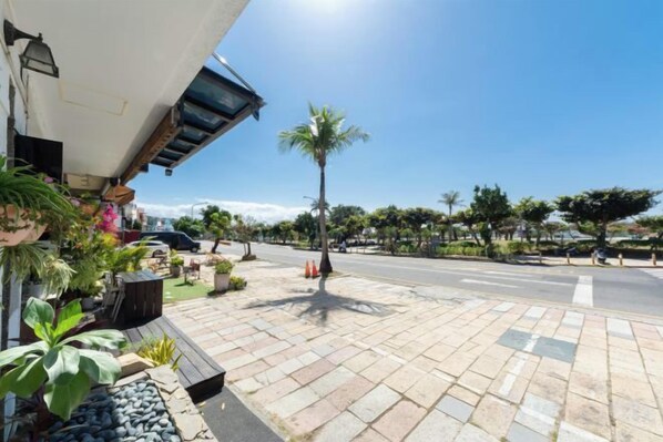 A paved outdoor area with a palm tree, a street, and a building with a slanted roof. - Kenting Lan Bay Hotel (Pingtung)