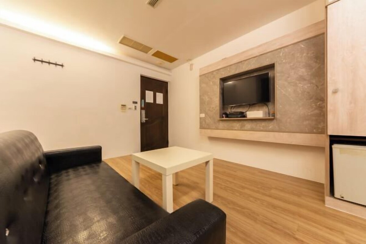 Un salon moderne avec un canapé en cuir noir, une table basse blanche et un téléviseur à écran plat fixé à un mur en marbre.