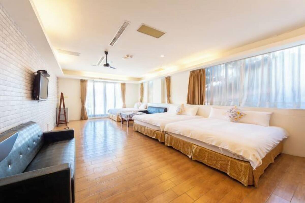 A hotel room with a large bed, a sofa, a TV mounted on the wall, and a window with curtains.