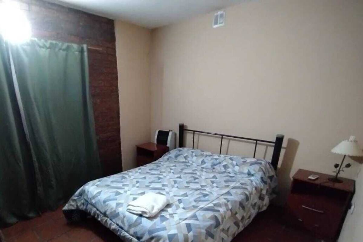 Une chambre à coucher avec un lit, une table de chevet, une lampe, un haut-parleur et un rideau.