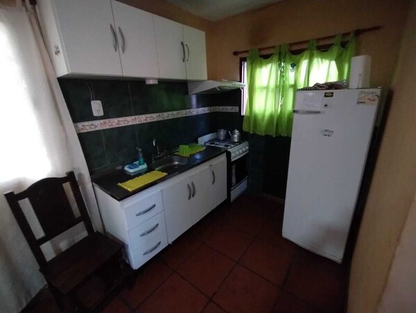 A compact kitchen with white cabinets, a stove, a sink, and a refrigerator. - puertas del sol (Los Molles)