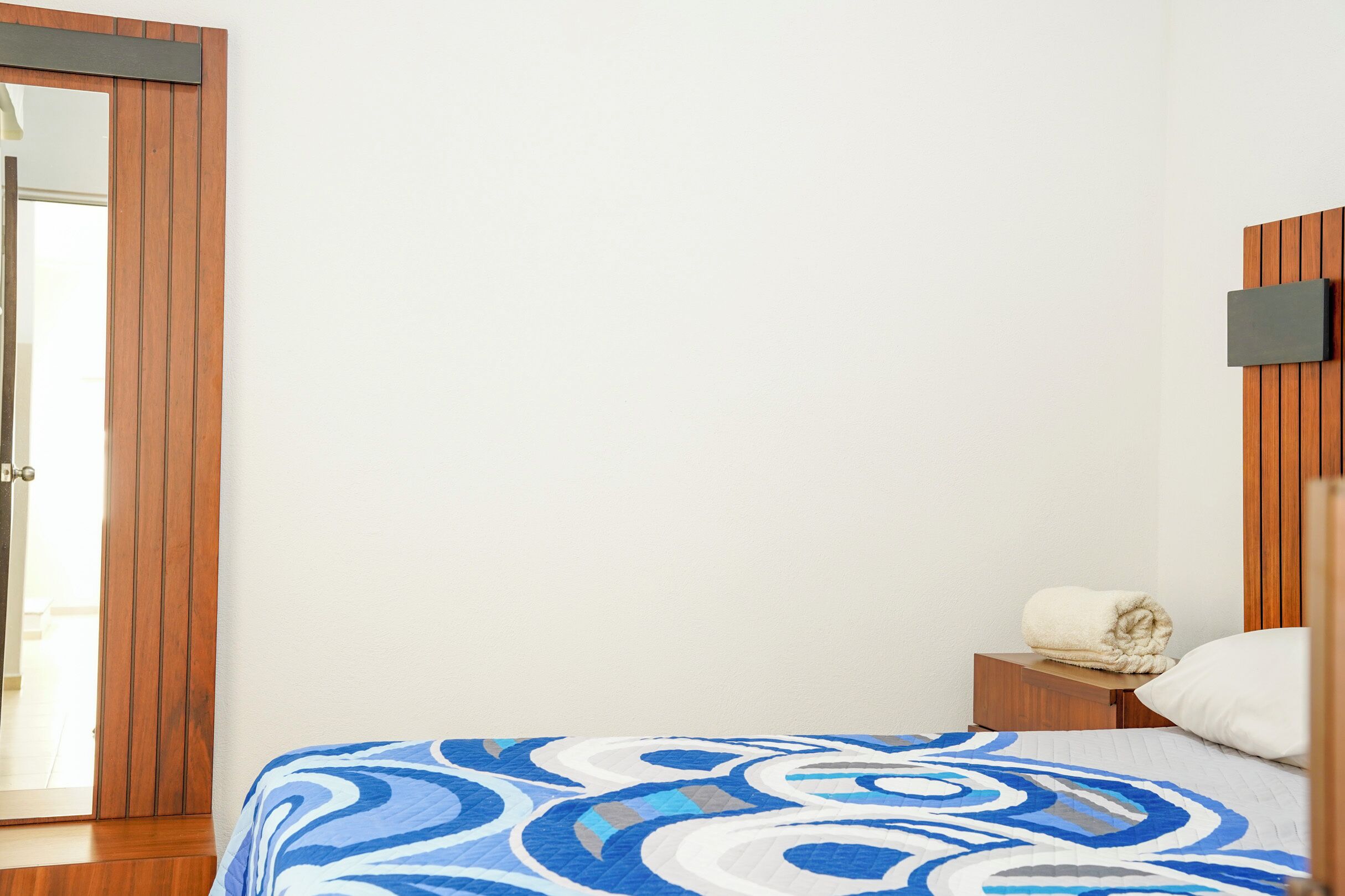 A bedroom with a bed, a wooden nightstand, a white pillow, and a wall-mounted TV.