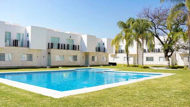 Un bâtiment moderne doté d’une piscine, de murs extérieurs blancs et de balcons avec des garde-corps noirs.