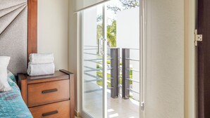 Une chambre avec une table de chevet en bois, un lit recouvert d’une courtepointe et une porte-fenêtre coulissante donnant sur un balcon doté d’une rambarde en métal.