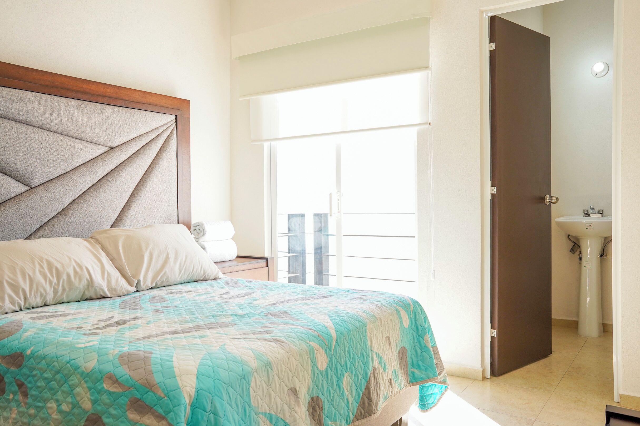A bedroom with a bed, a window, and a bathroom visible through an open door.