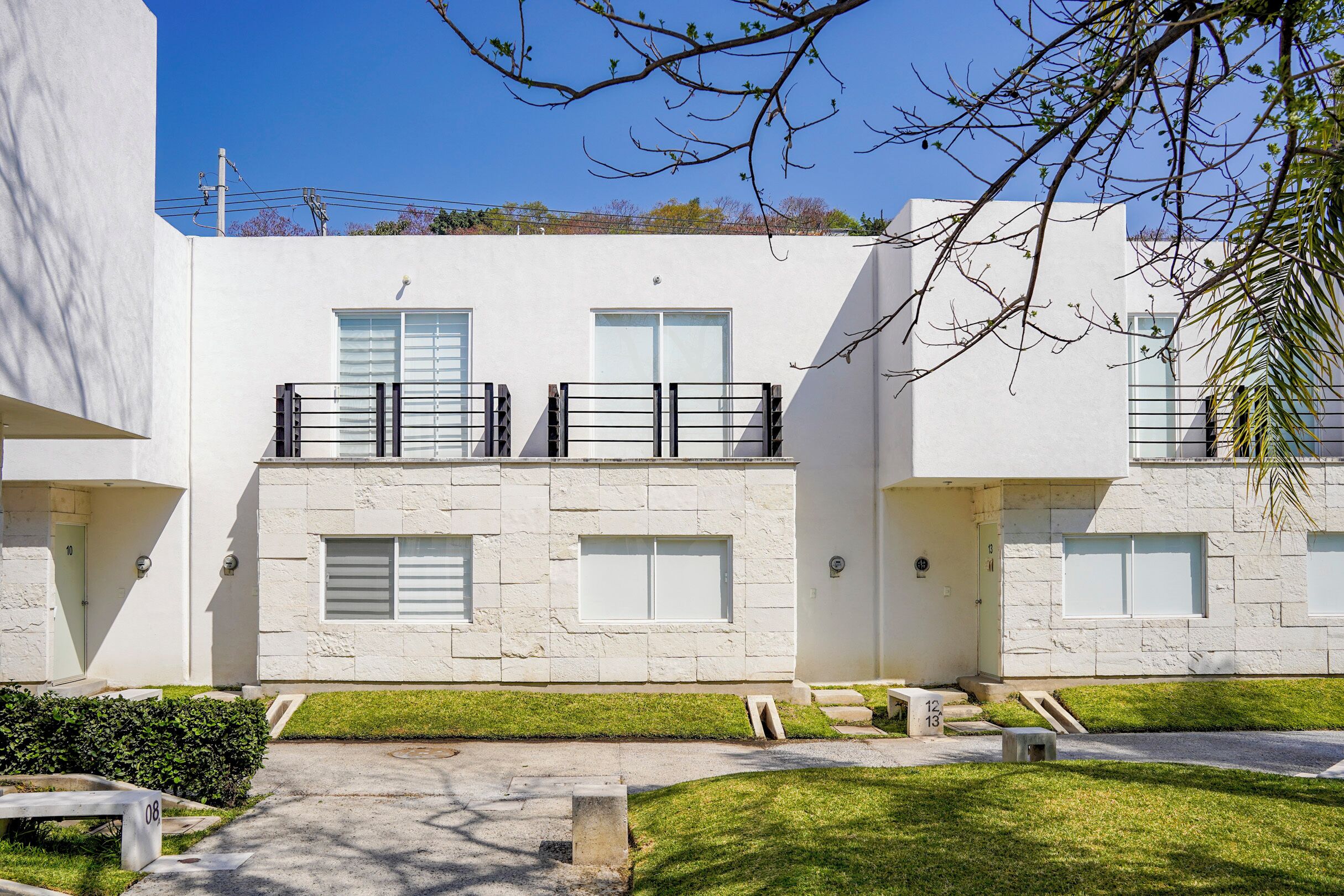 A modern two-story building with a clean, white facade, large windows, and a small balcony on the upper floor.