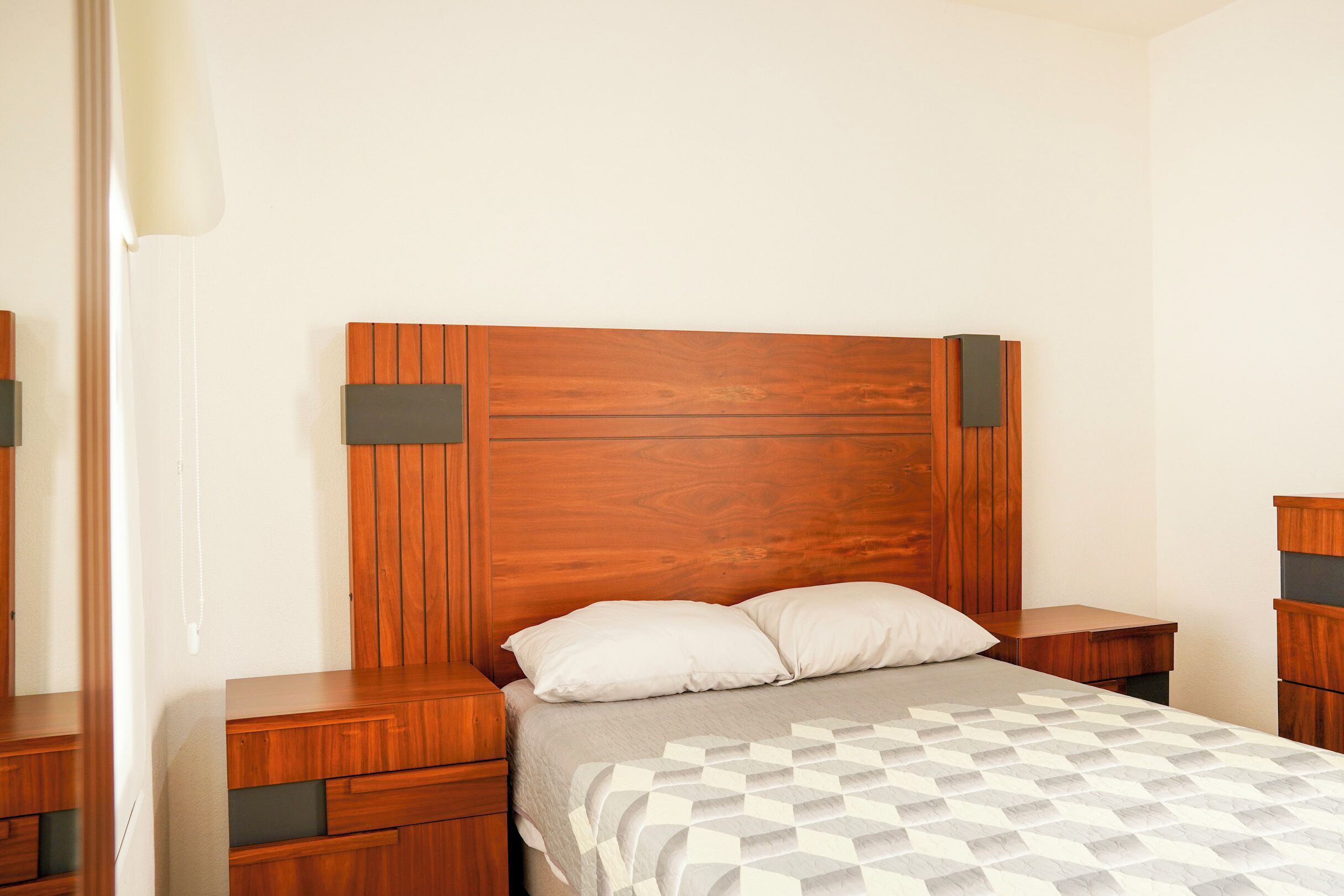 A bedroom with a wooden headboard, a bed with a patterned bedspread, and wooden nightstands.