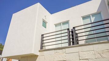 A modern building with a white facade, a small window, and a balcony with a metal railing.