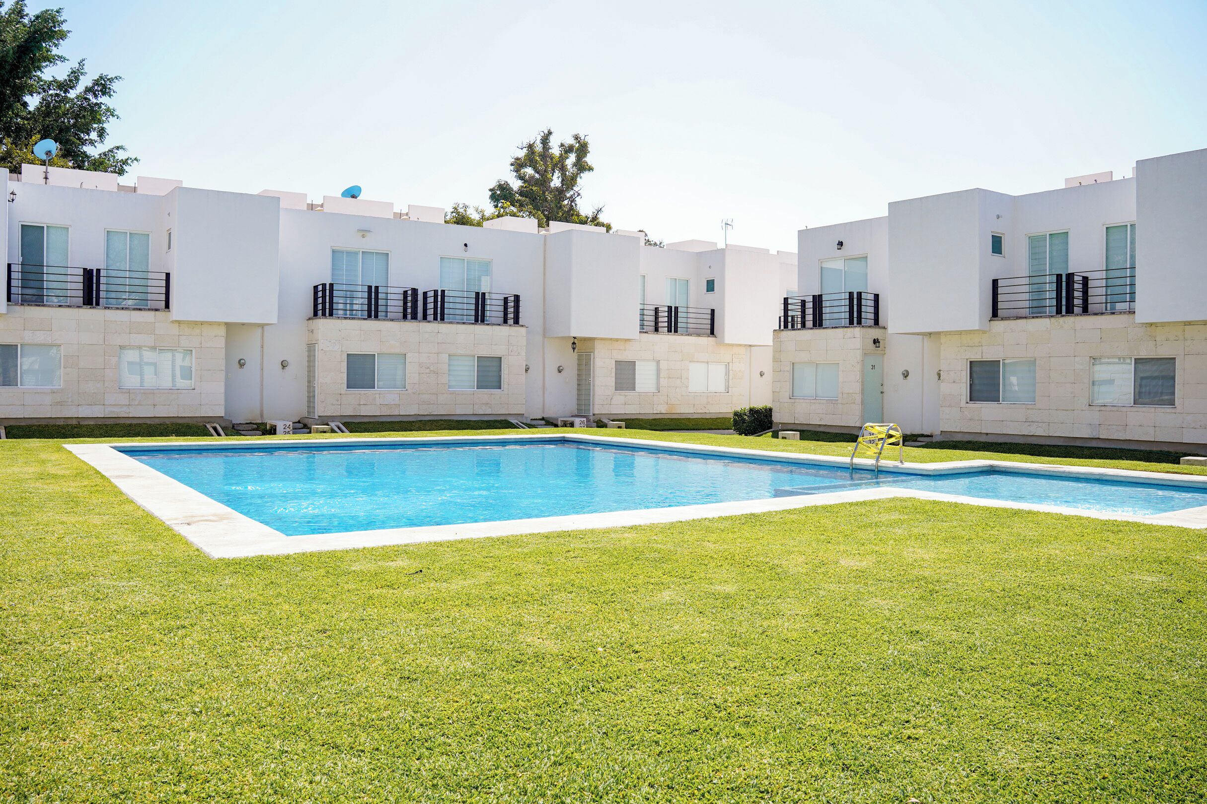 A modern apartment complex with a swimming pool, flat-roofed buildings, and satellite dishes.