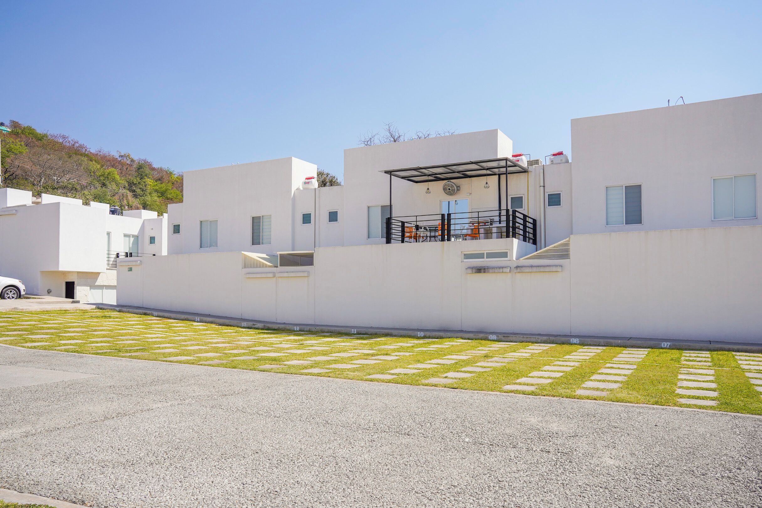 Un bâtiment moderne doté d’un toit plat, d’un espace extérieur couvert aménagé en coin salon et d’un chemin piétonnier pavé.