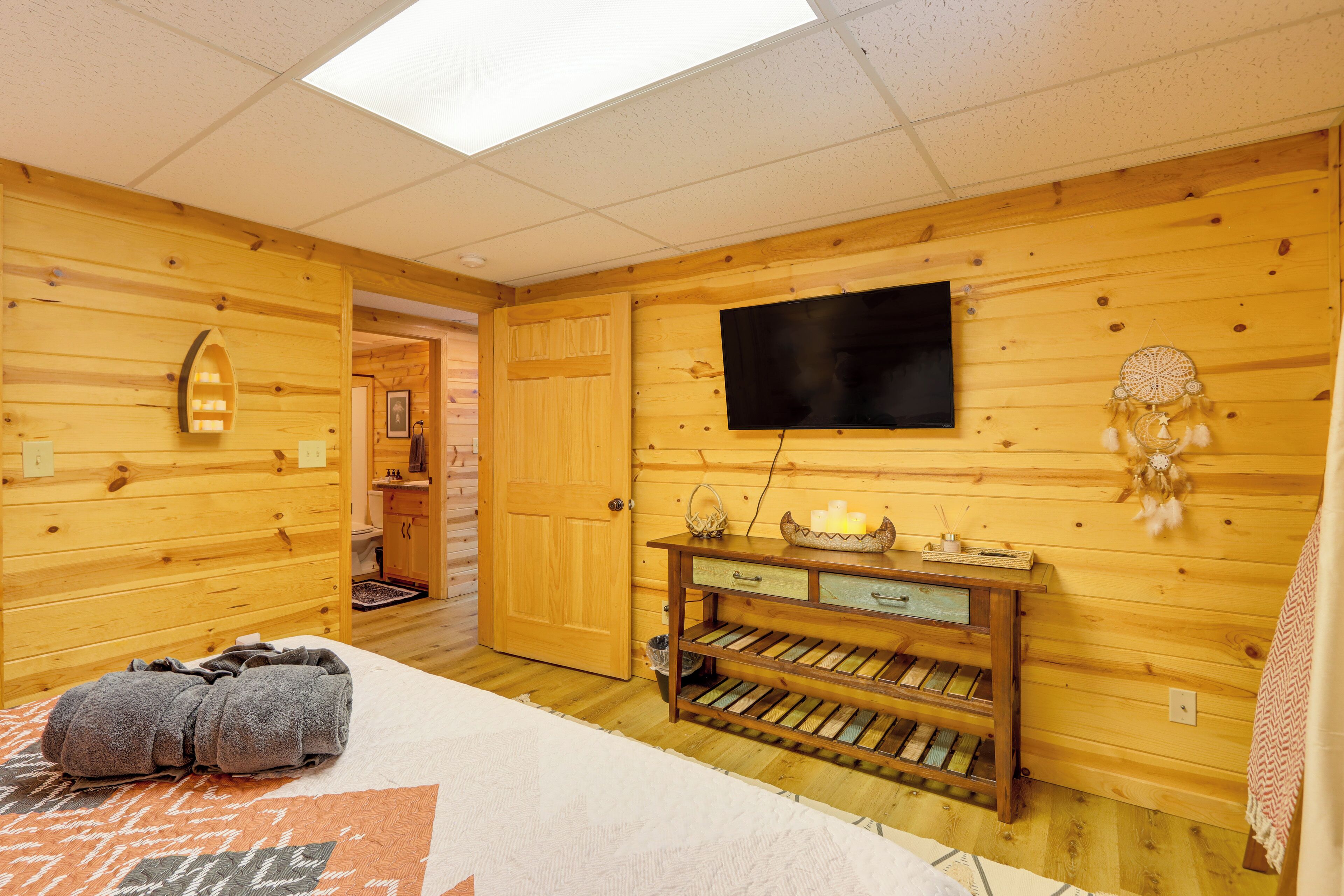 A wooden room with a bed, a TV mounted on the wall, and a small table with decorative items.