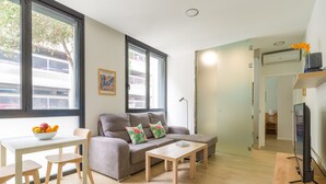 A modern living room with a grey sofa, a white table with a fruit bowl, and a TV on a wooden stand. - VIVENTE 3B BY CANARIAS GETAWAY (Las Palmas de Gran Canaria)