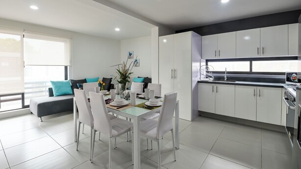 A modern kitchen with white cabinets, a dining area with white chairs, and a grey sofa with teal cushions. - Beautiful apartment near the beach (Boca del Rio)