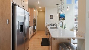 A modern kitchen with stainless steel appliances, wooden cabinets, a large island with a sink, pendant lighting, and a view of the outdoors. - 3min Walk to Ski Lifts*Hot Tub*Sauna*Views (Brian Head)
