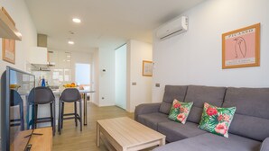 Eine moderne Wohnung mit grauem Sofa, einem Holztisch und einer Küchenzeile inklusive Esstisch und Stühlen.