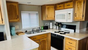 A compact kitchen with wooden cabinets, a built-in microwave, a gas stove, and a sink. - The Rolling Rogue Cabin #49 (Gold Beach)