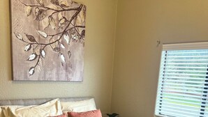 A bedroom with a bed, pillows, a nightstand, a potted plant, and a window with blinds. - The Rolling Rogue Cabin #49 (Gold Beach)