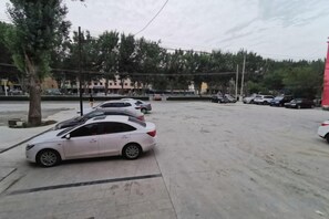 A parking lot with several cars parked, trees, and a building in the background. - Hutubi Xintian Hotel (Hutubi)
