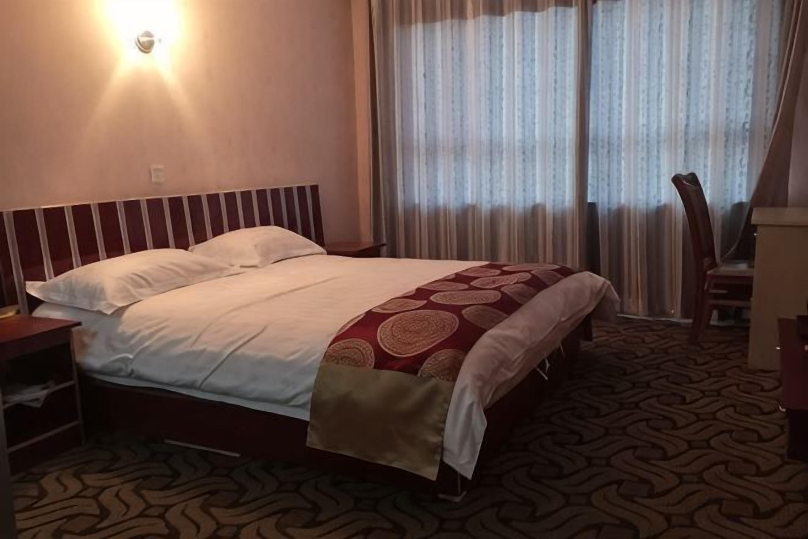A hotel room with a bed, a nightstand, a chair, and a desk.