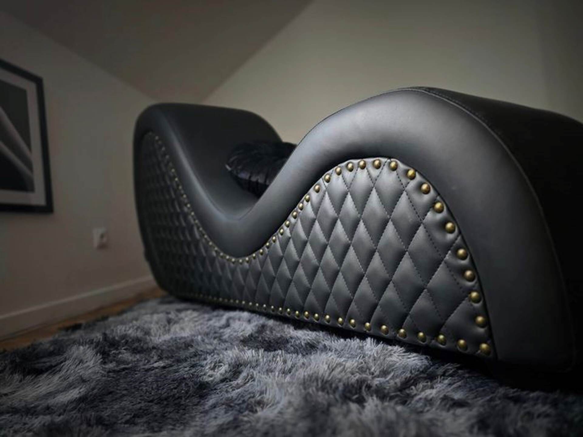 A black leather sofa with a quilted pattern and gold studs, placed on a gray furry rug.