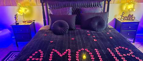 Ein Bett mit Rosenblättern, die das Wort „AMOUR“ bilden, und einer Kerze darauf.