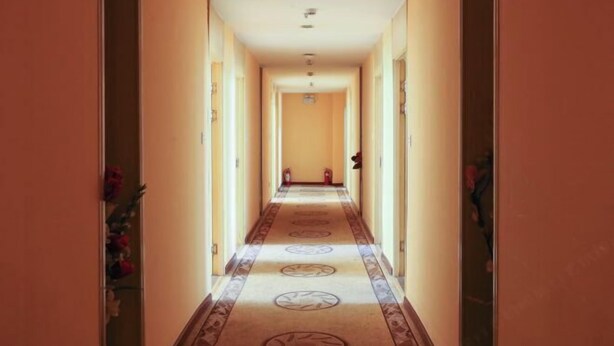 A long, narrow hallway with a patterned carpet and a central fire extinguisher. - OYO Jingbian County Tianli Holiday Hotel (Jingbian County)