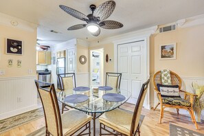 A dining area with a glass table, wicker chairs, a ceiling fan, and a wicker chair with a cushion. - Fernandina Beach Condo w/ Pool + Path to Beach! (Fernandina Beach)