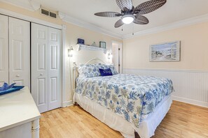 A bedroom with a bed, a desk, a ceiling fan, a door, and a wall-mounted shelf. - Fernandina Beach Condo w/ Pool + Path to Beach! (Fernandina Beach)