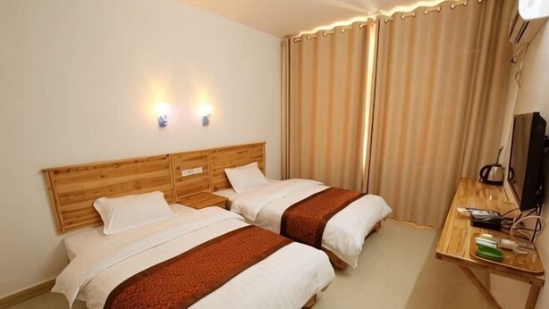 A hotel room with two beds, a desk, a television, and a window with curtains. - Wonton Hotel Yangshuo (Yangshuo)