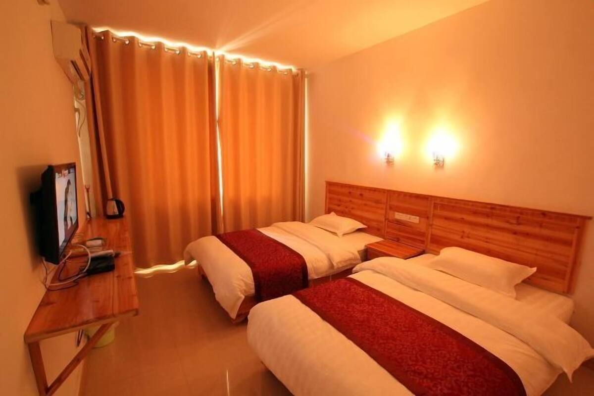 A hotel room with two beds, a wooden headboard, a desk with a television, and two wall-mounted lights.