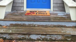 A blue door with a glass panel, a clawfoot bathtub, and a doormat with "Wipe Your Claws" text.