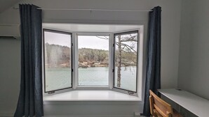 A room with a bay window overlooking a lake and trees.