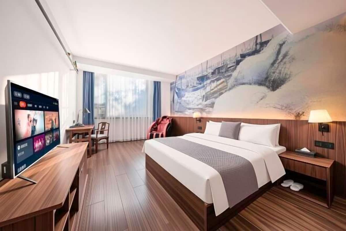 A hotel room with a large bed, a desk, a TV, and a painting on the wall.