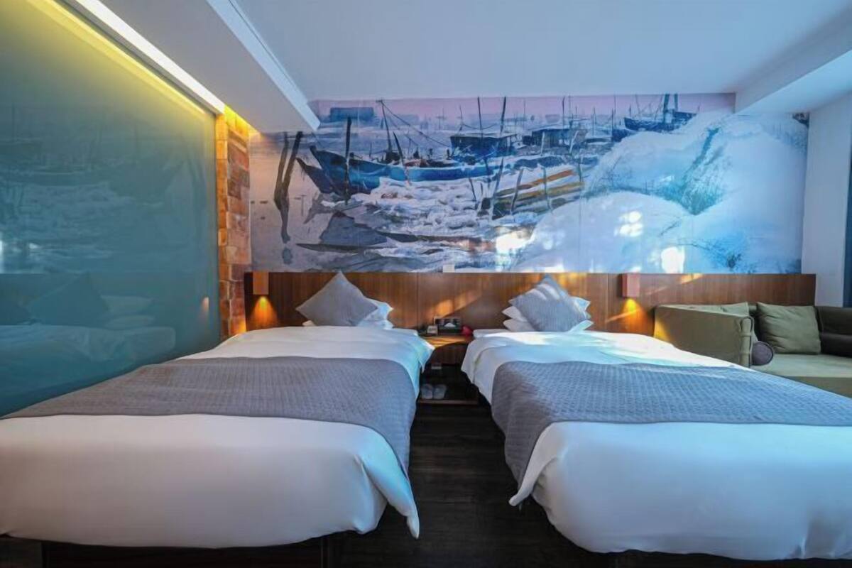 A hotel room with two beds, a large painting of boats, and a wooden headboard.