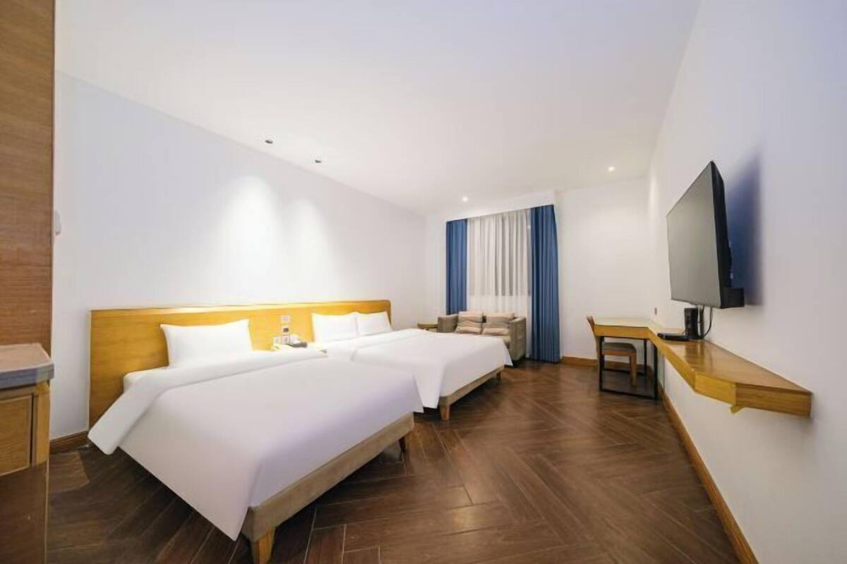 A hotel room with two beds, a desk, a chair, a TV, and a window with curtains.
