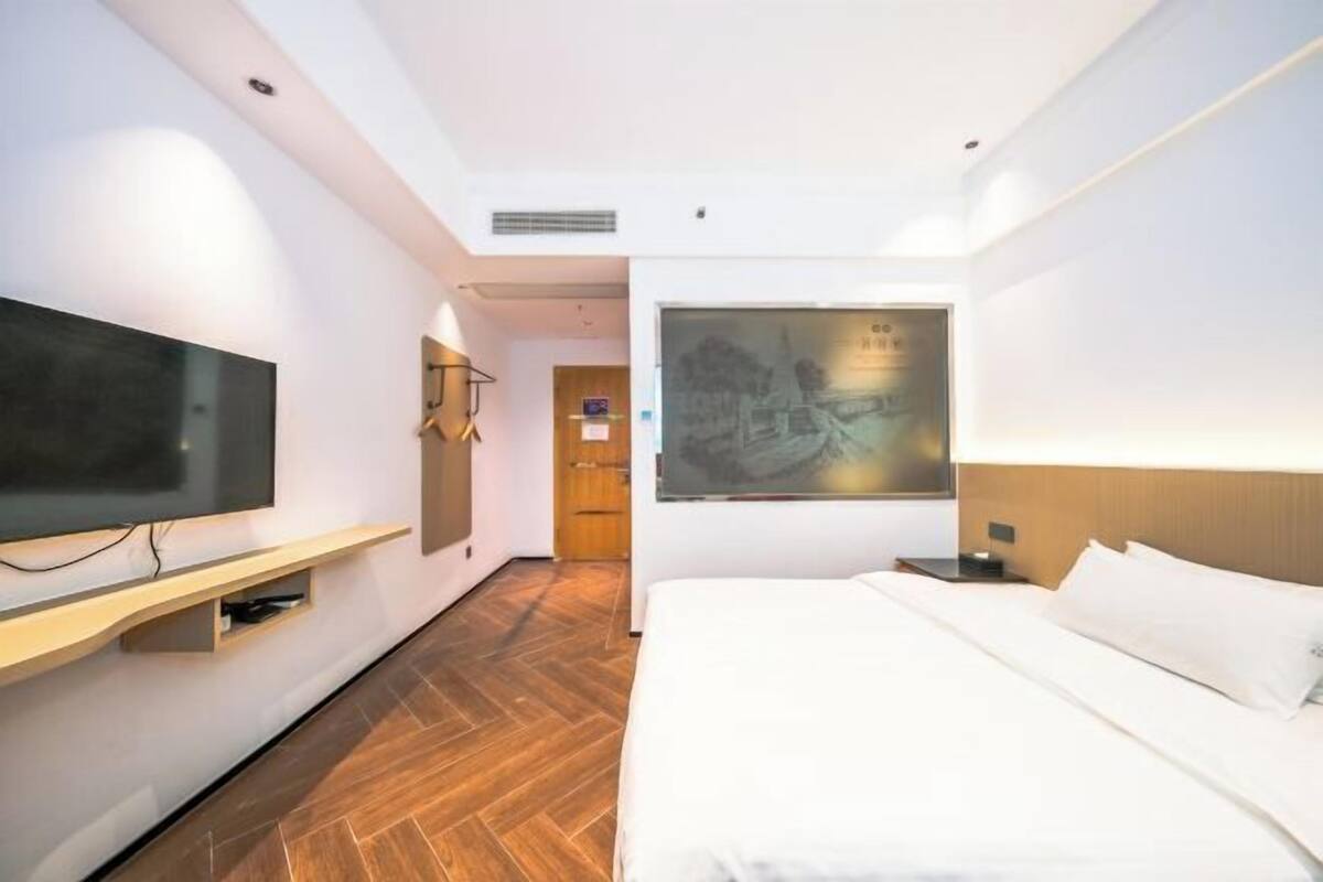 A hotel room with a bed, a flat-screen TV, a wall-mounted artwork, and a wooden floor.