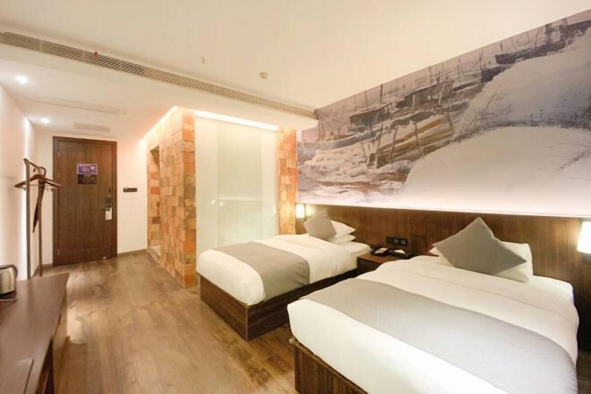 A hotel room with two beds, a wooden floor, a large painting of a snowy landscape, and a door with a sign.