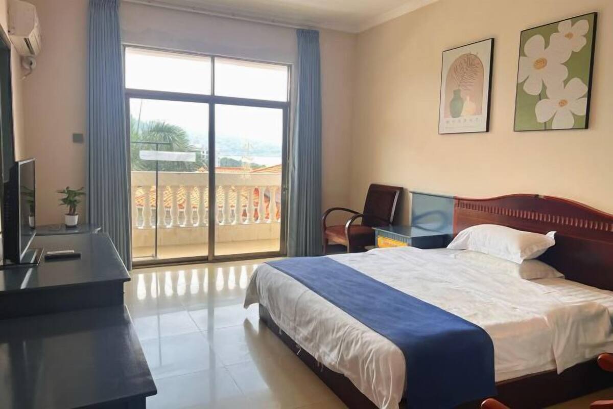 A hotel room with a bed, a desk, a chair, a TV, and a balcony with a view.