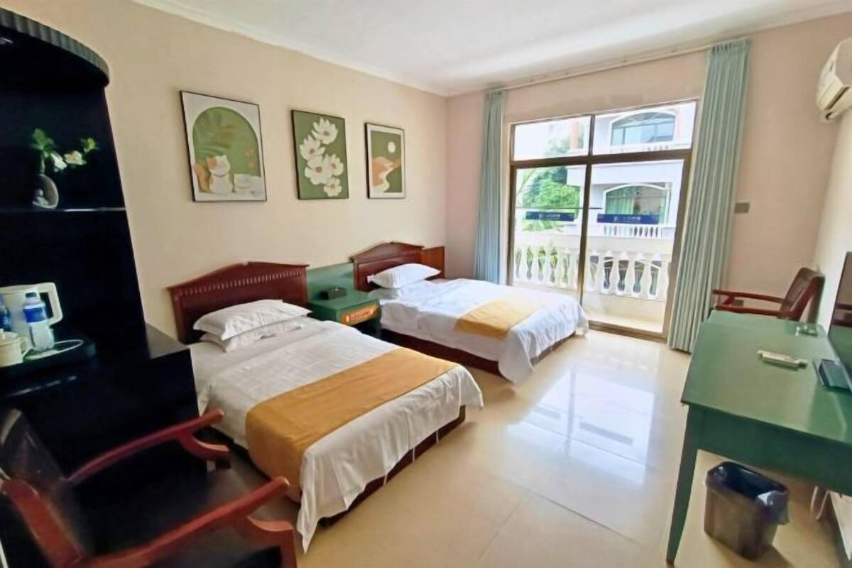 A hotel room with two beds, a desk, a chair, a TV, and a balcony with a railing.