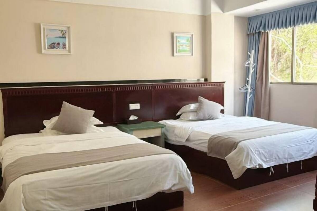 A hotel room with two beds, a wooden headboard, a nightstand, and a window with curtains.