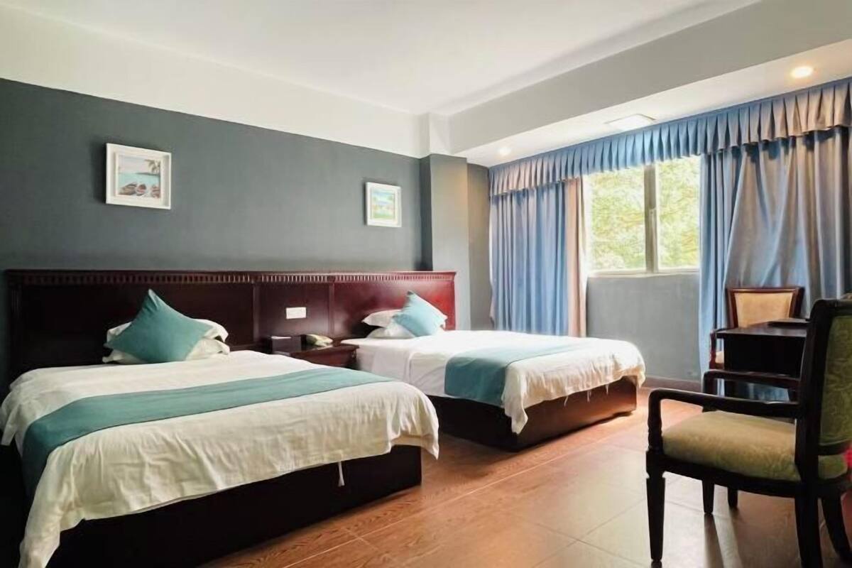A hotel room with two beds, a wooden headboard, a chair, and a window with curtains.