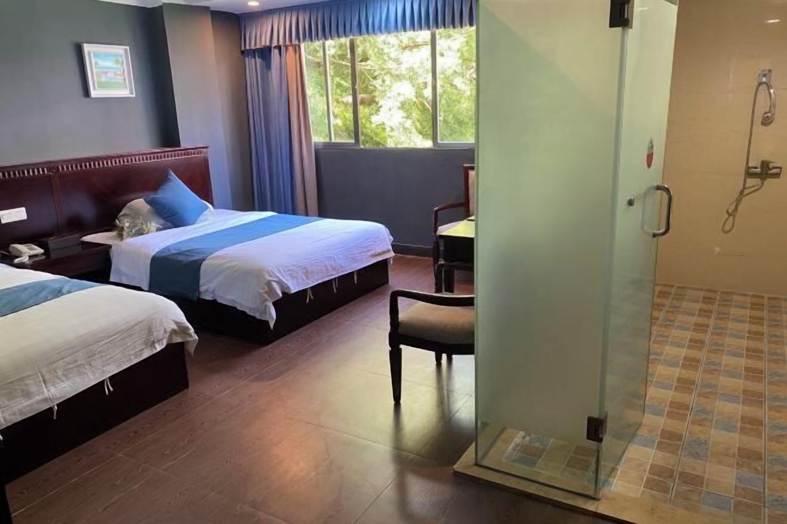 A hotel room with two beds, a shower area, and a view of greenery outside.