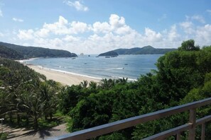 Un paysage côtier avec une plage, l’océan et des collines boisées.