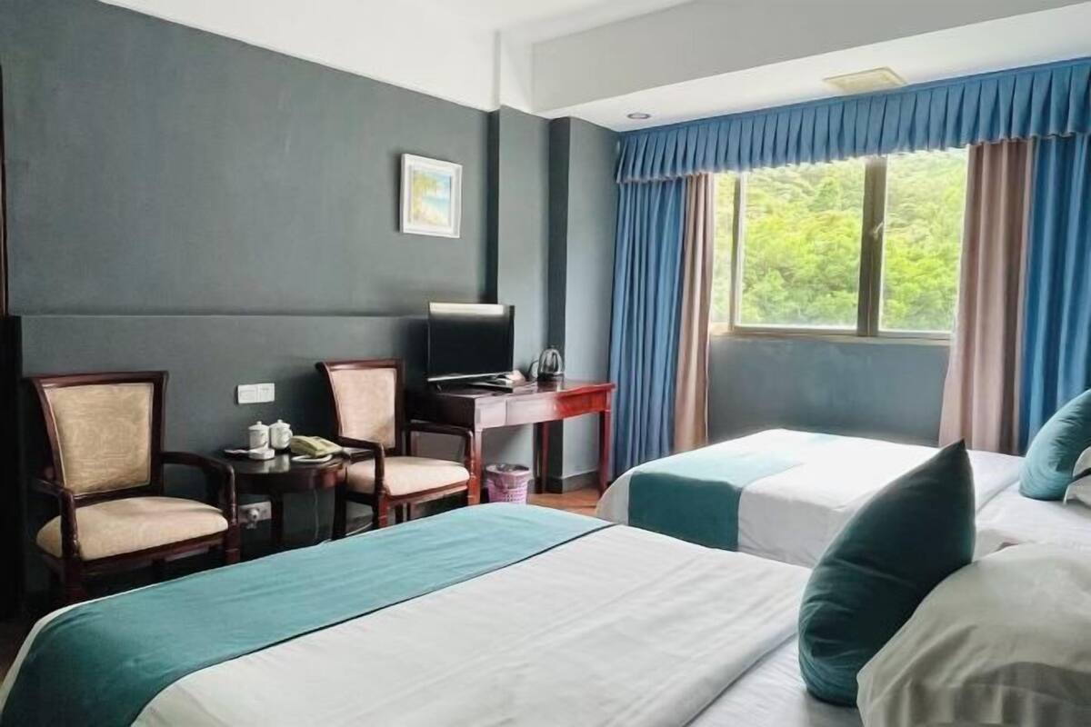 A hotel room with two beds, a desk, chairs, and a window with curtains.
